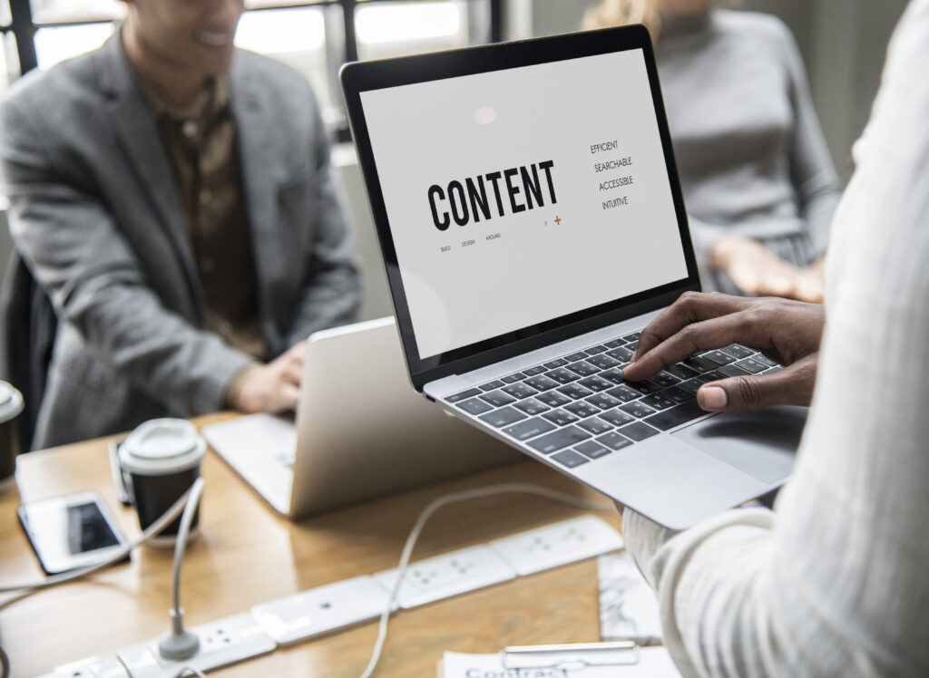 A person holding a laptop displaying the word "CONTENT" while two people work on laptops in the background, illustrating Weblook International's website content creation services in Sri Lanka.